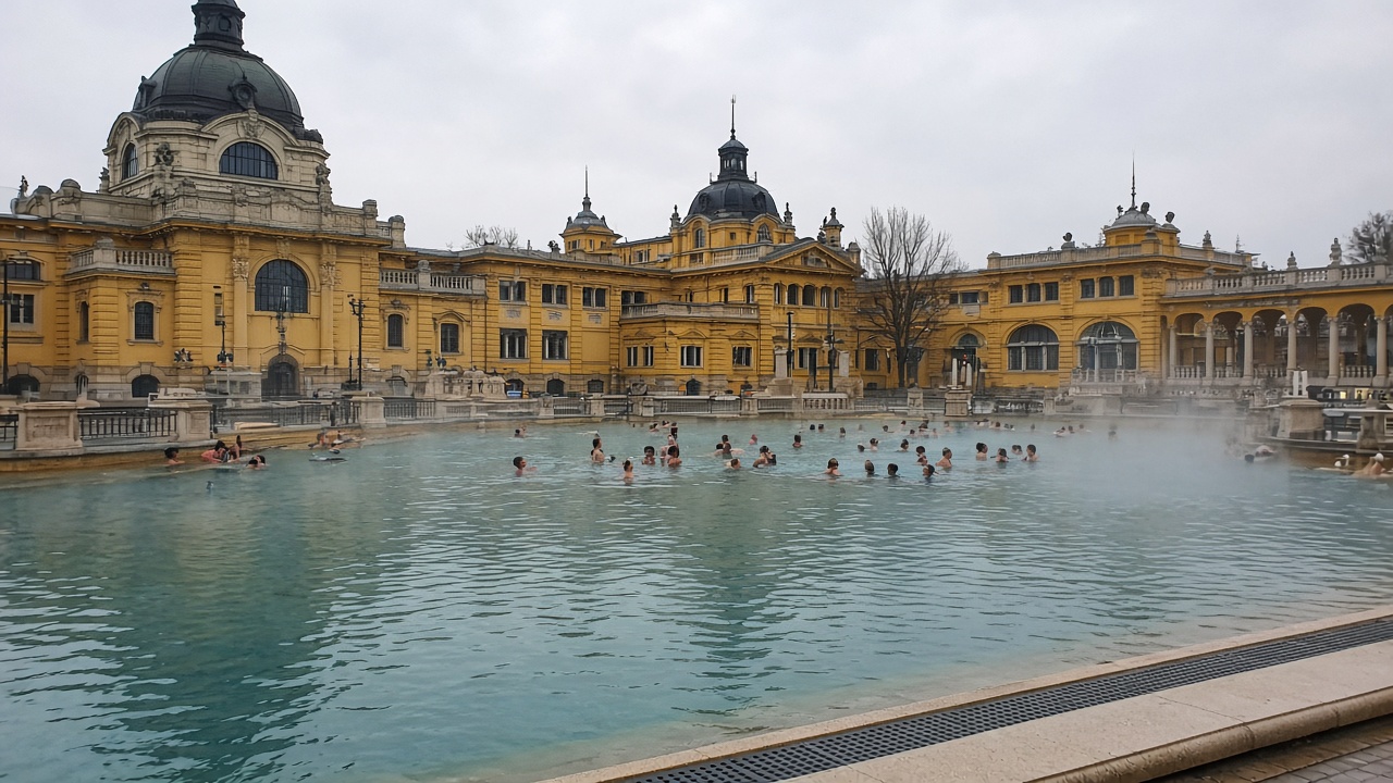 Tourist phone photo of Széchenyi Thermal Bath outdoor pools steaming beside yellow neo-Baroque buildings, Budapest