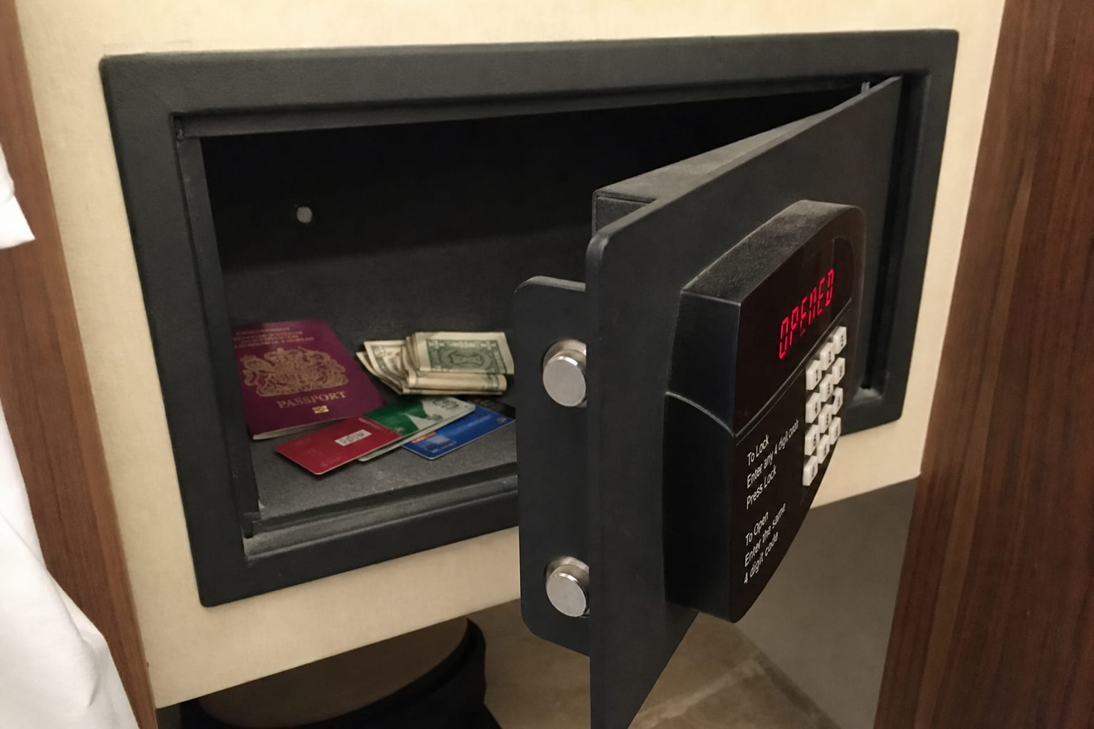Phone snapshot: open in-room hotel safe with passport, cards, and folded cash inside