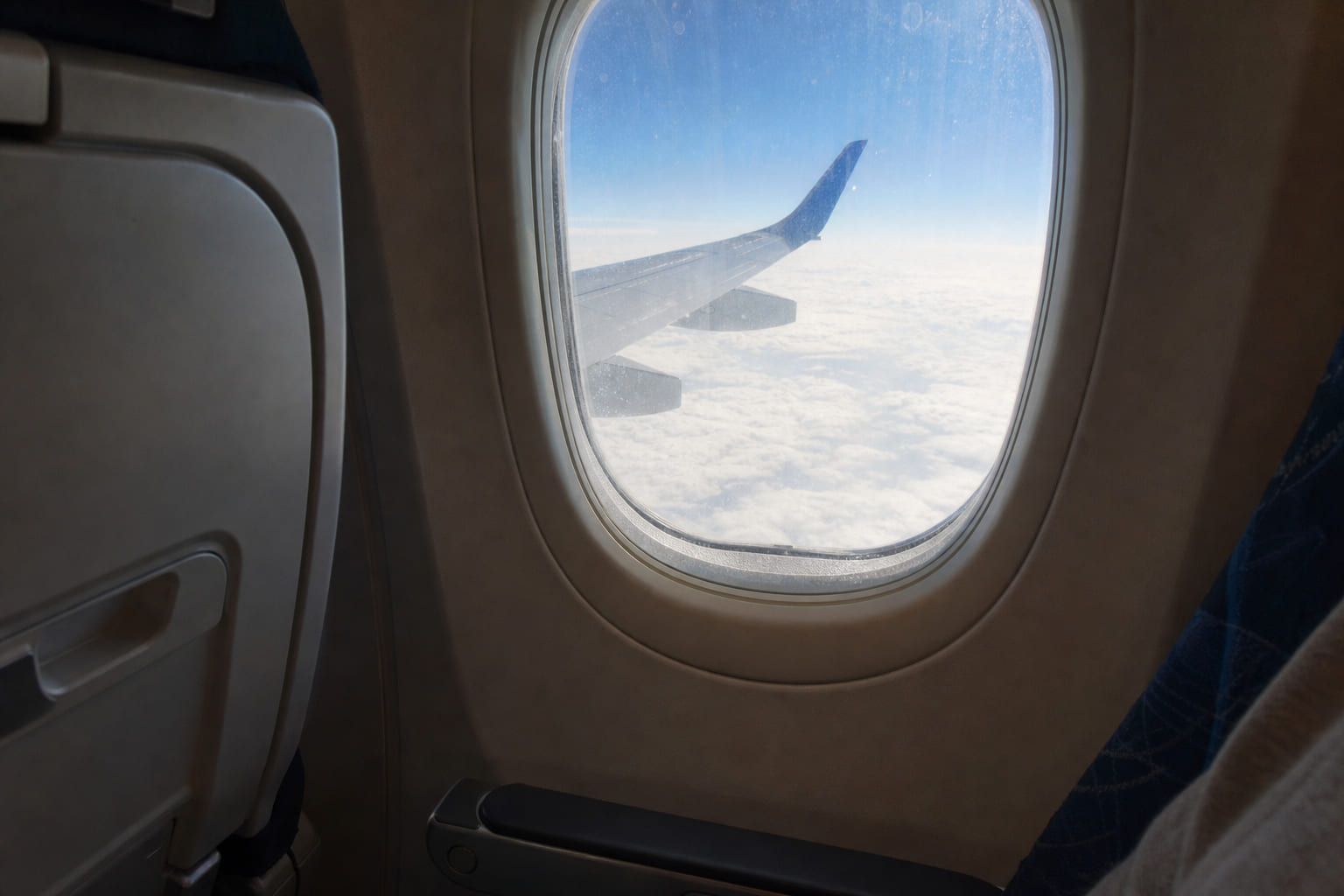 Casual phone photo from an airplane window seat: wing over clouds, armrest and seatback in frame